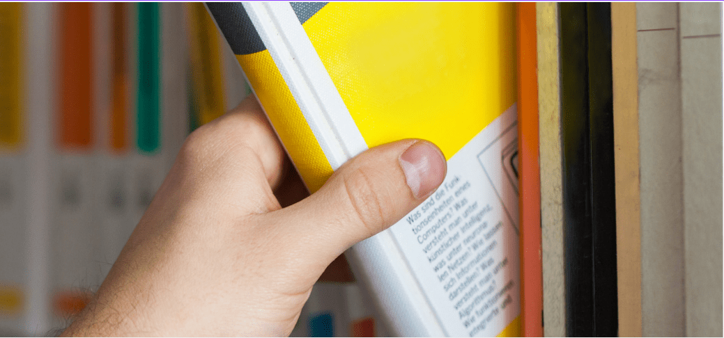 Pile of books with an apple on top in a classroom. Pencils and ABC blocks are visible